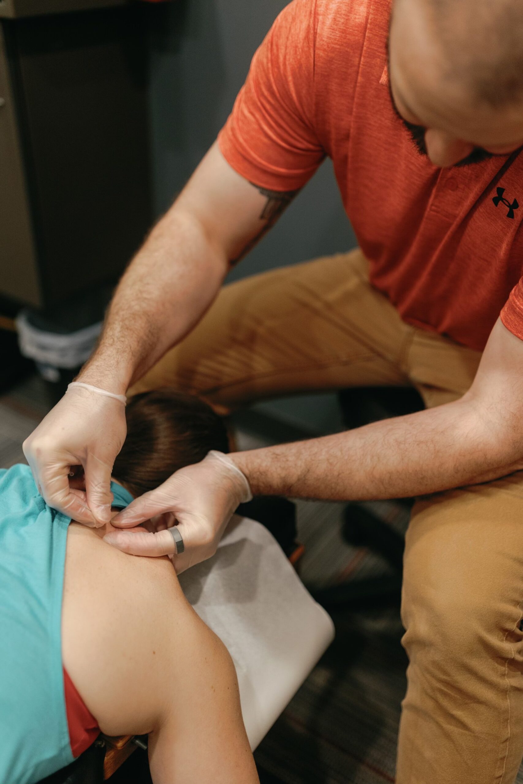 Patient lays facedown on a table as a practitioner in medical gloves carefully places acupuncture needles. 