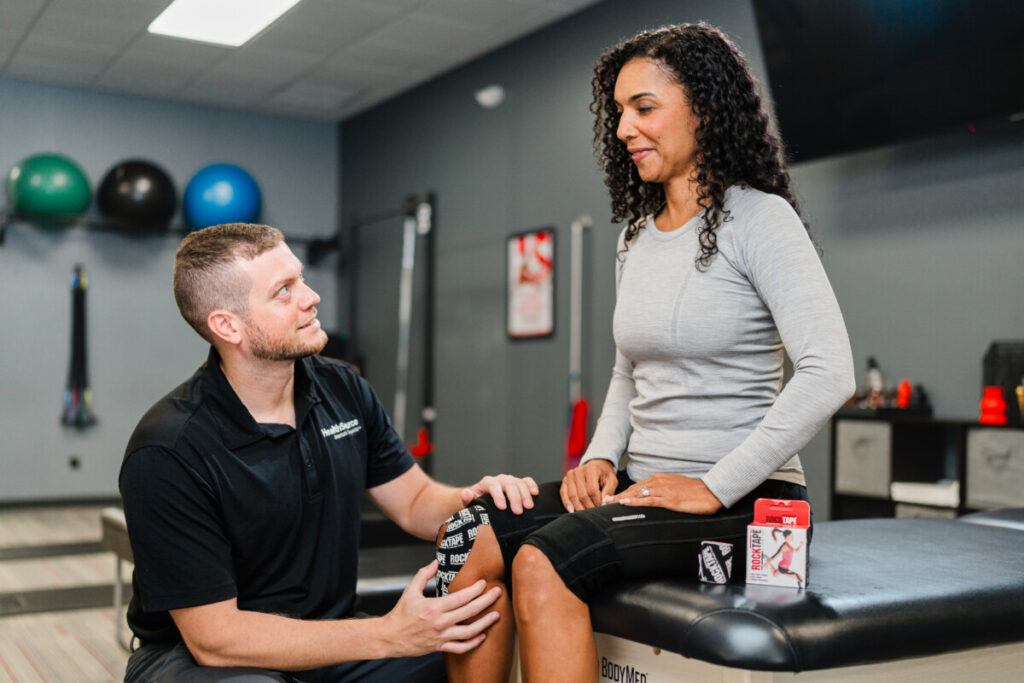 Practitioner checks with patient as they place kinesiology tape on her knee.