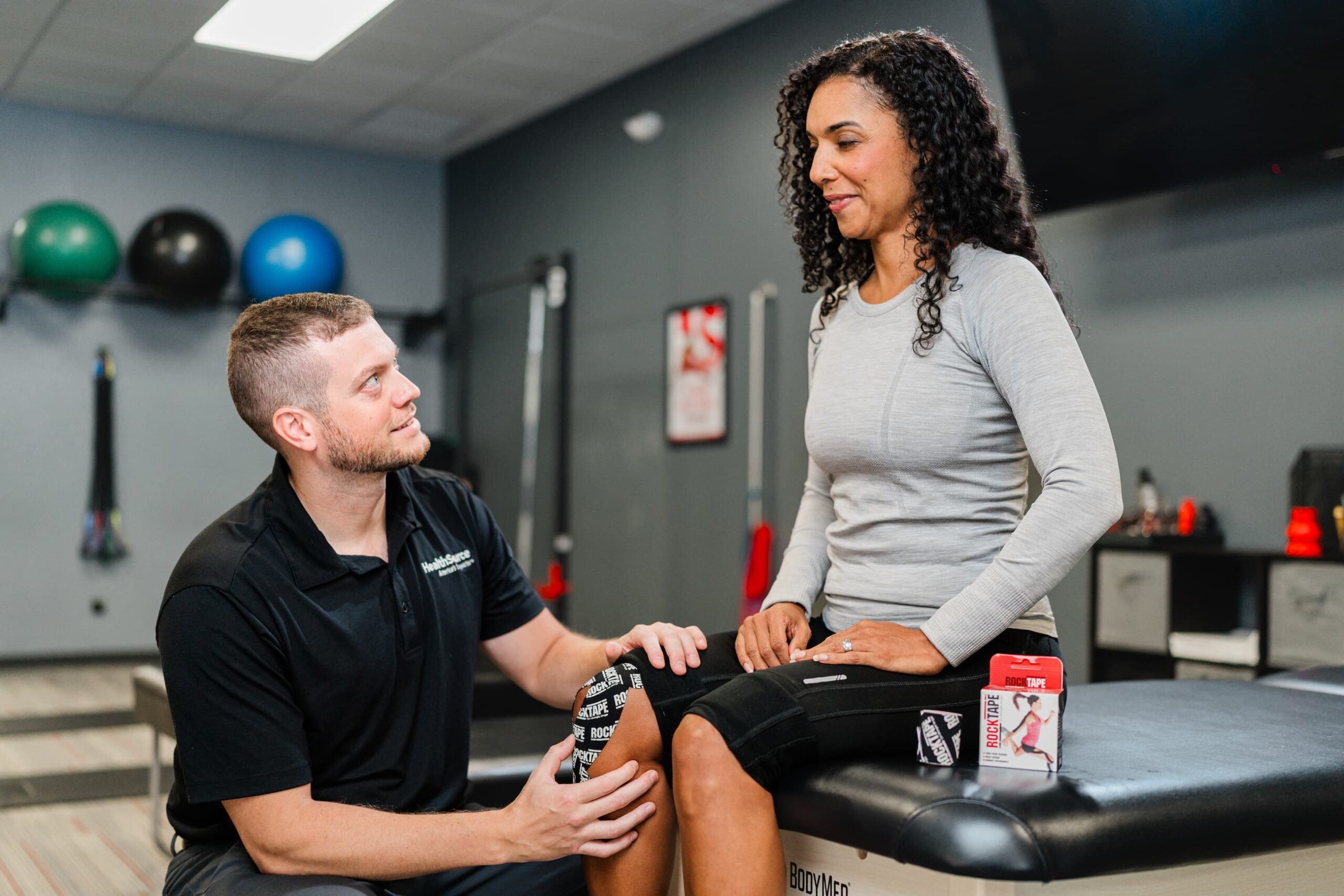 Practitioner checks with patient as they place tape on her knee.