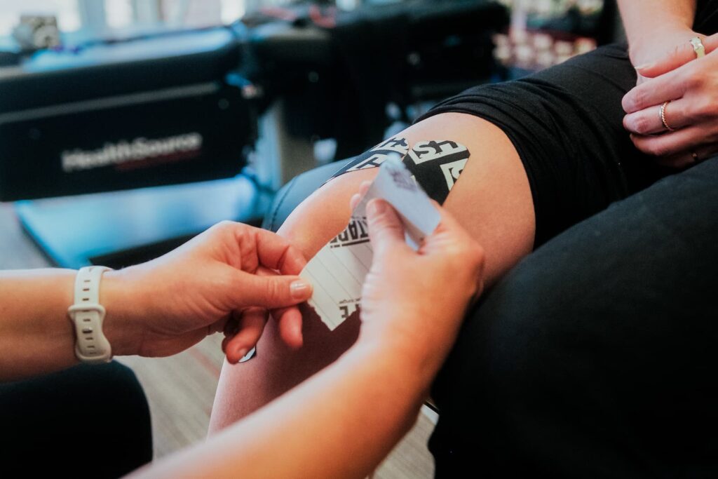 Close up of practitioner peeling the backing off tape as they place it down the side of their knee.