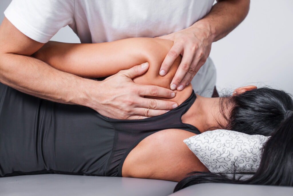 A patient lays on their side on a table; a practitioner massages their left shoulder blade.