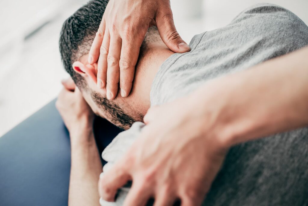 Close up of patient on table; a practitioner carefully massages the upper half of their neck.