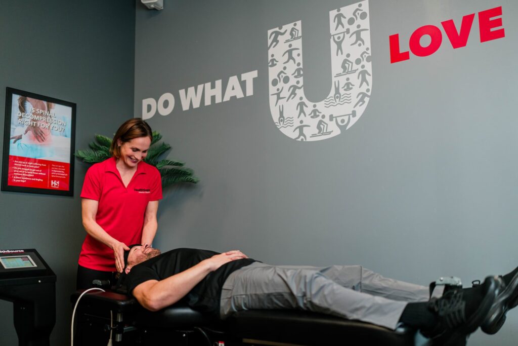 Wide view of a practitioner working on the neck of a patient who is laying down on a table.