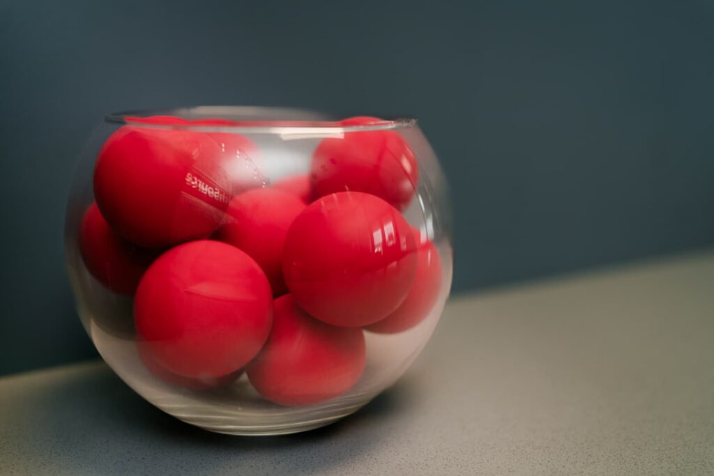 Small red exercise balls collected in a glass fishbowl, sat on a countertop.