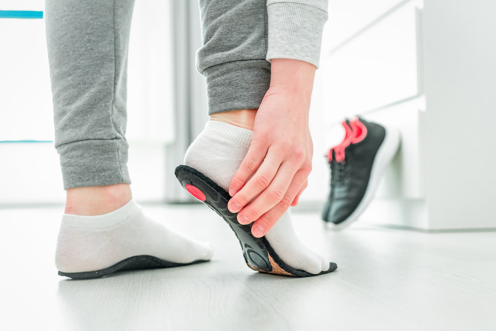 Close up of a person pressing an orthotic against their sock-covered foot, testing its fit before putting their shoes on.