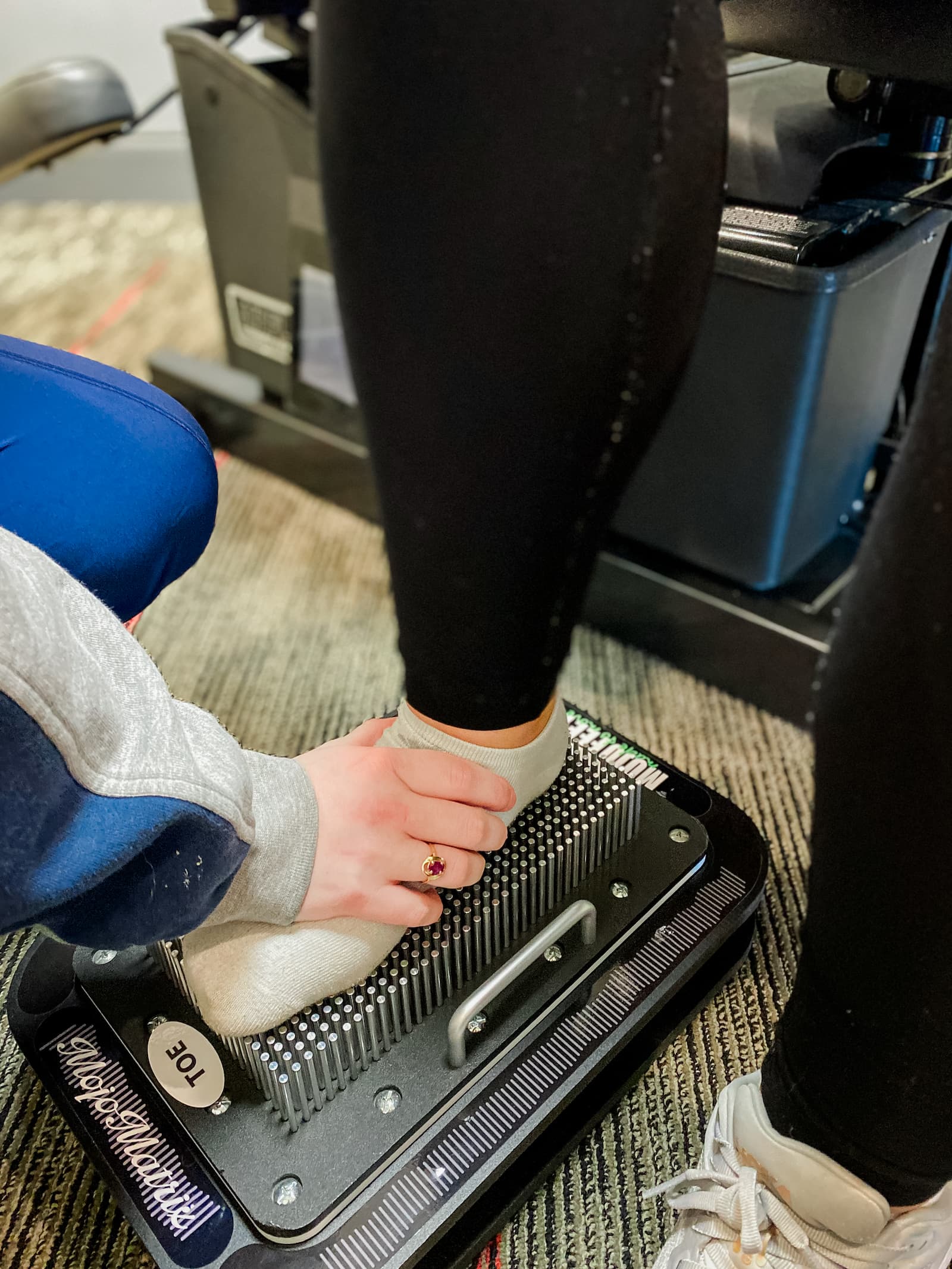 Patient presses foot into tool that takes an impression. A practitioner helps by holding their foot even. 