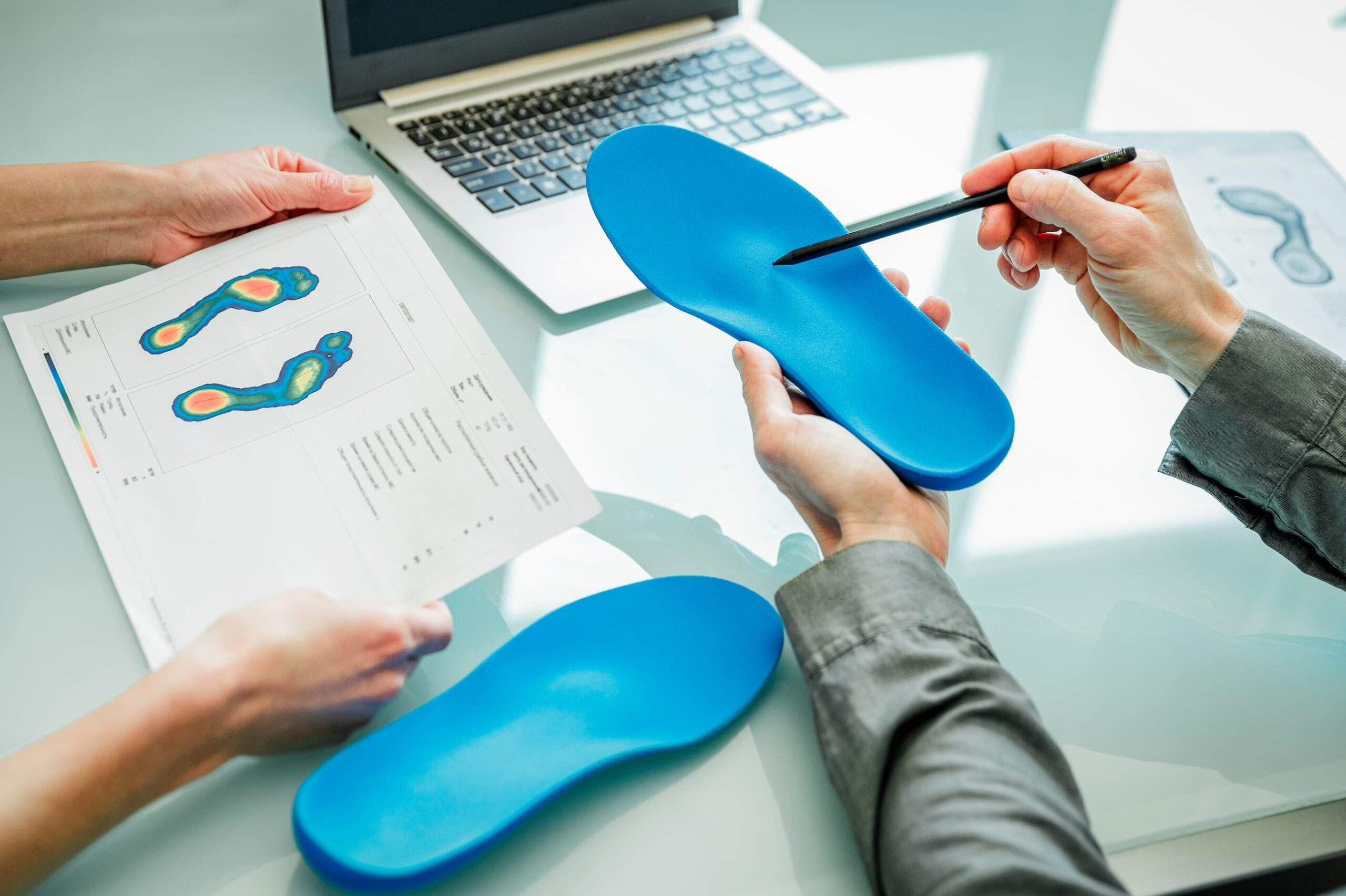 Close up of practitioner pointing to the top half of a blue orthotic, as a patient reviews a document charting pressure points.