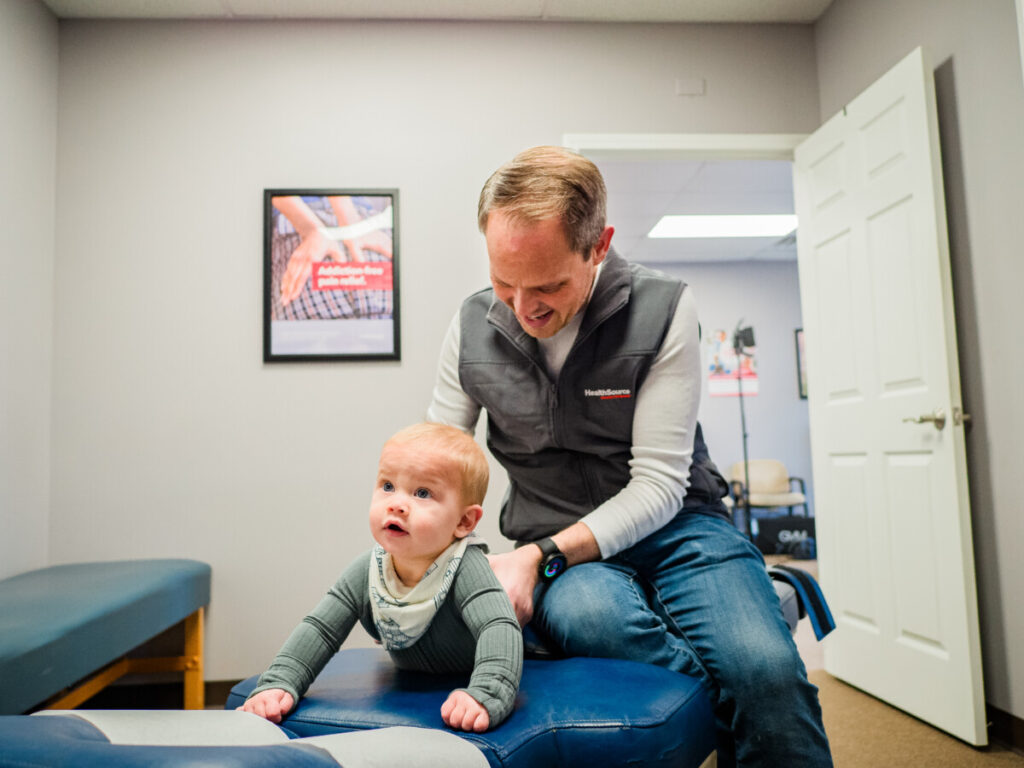 Chiropractor providing pediatric adjustment to an infant lying on their stomach