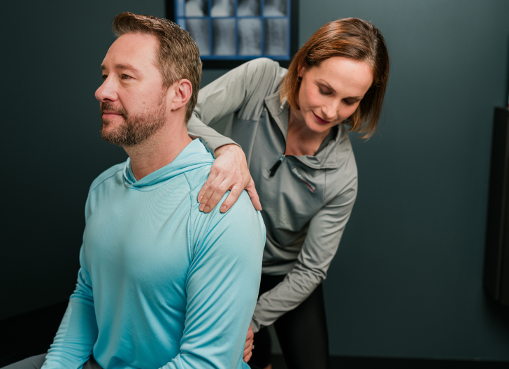 Patient sits straight as a practitioner holders their shoulder and lower back, adjusting.