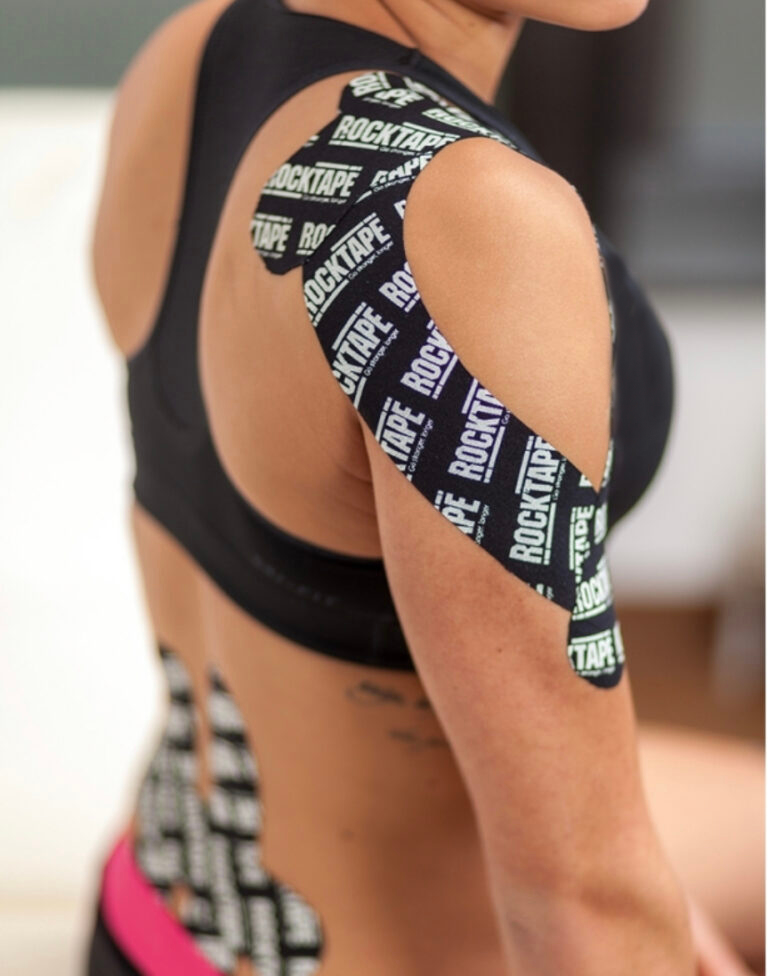 Close up of athletic woman's back and shoulder, wrapped carefully in black Kinesiology Tape.