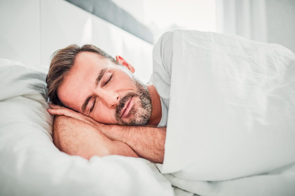 Close up of man sleeping comfortably on a white bed.