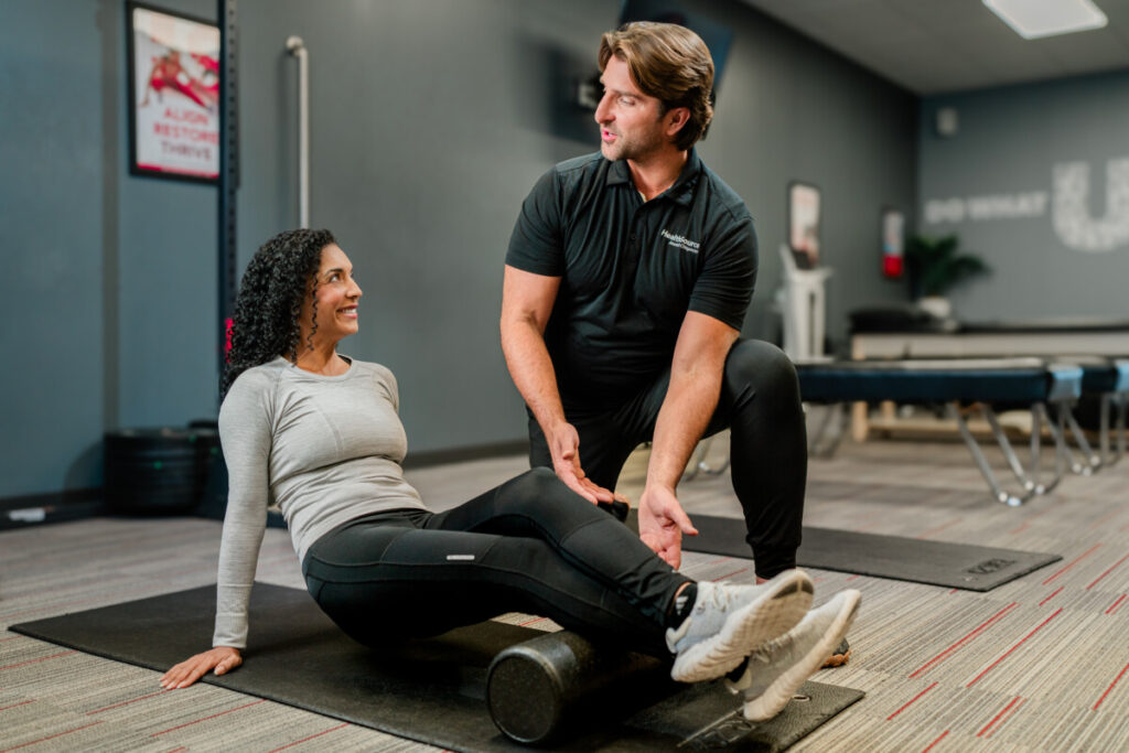 Patient smiles at employee as they use a foam roller during physical therapy