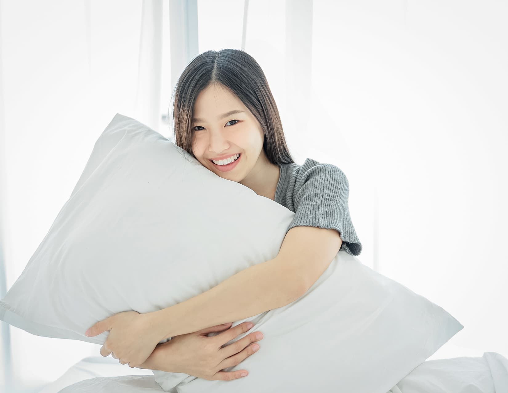 Woman smiles at the camera as she hugs a pillow.