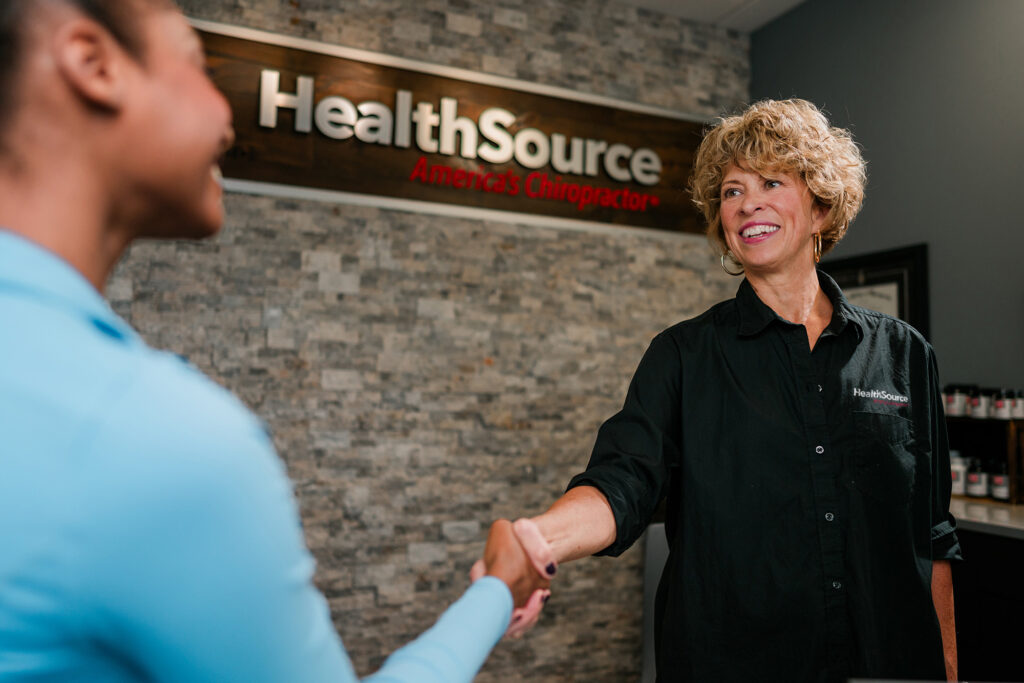 Front desk employee smiles as she shakes hands with a patient.