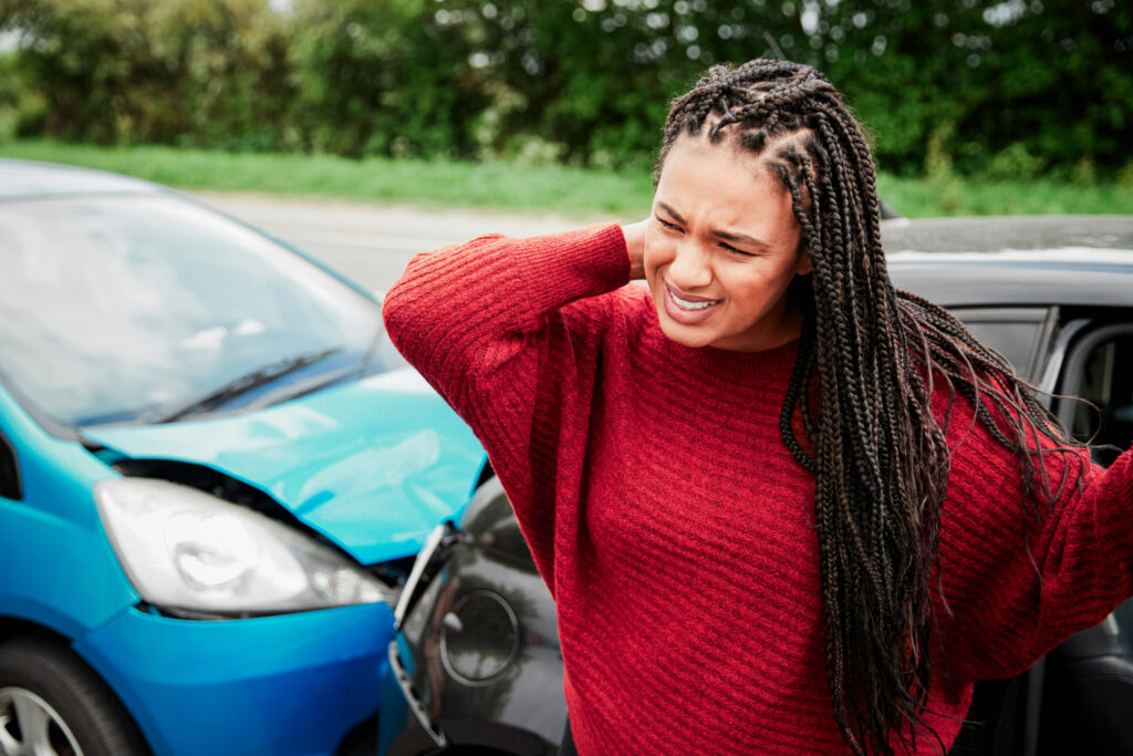 Female motorist with whiplash injury getting out of a crashed car.