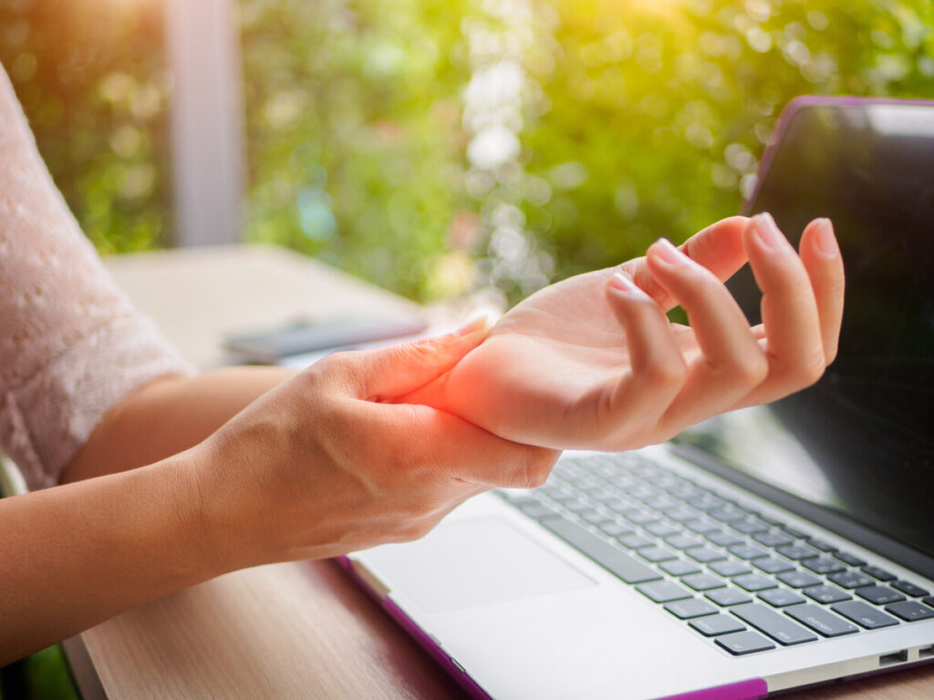 Closeup woman holding her painful hand experiencing carpal tunnel from using computer.