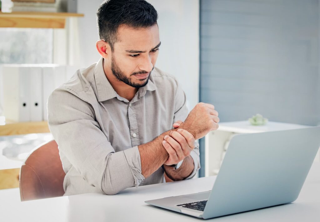 Man working at desk attempts to soothe carpal tunnel pain by massaging his wrist.