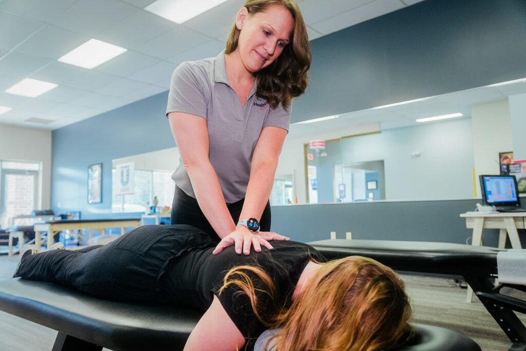 A HealthSource chiropractor stands over a patient on a table, carefully pressing into their back and shoulder.