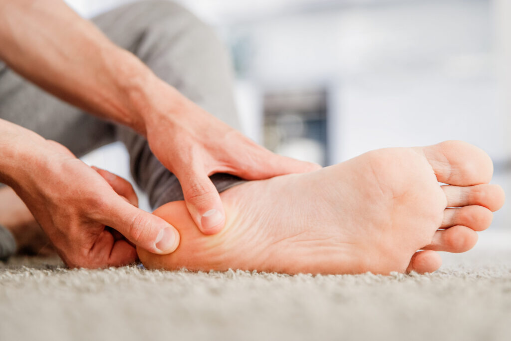 Man sits on the floor, massaging his bare heel.