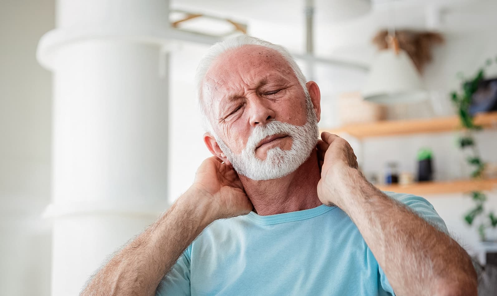 Senior man uses both hands to massage between his neck and head.