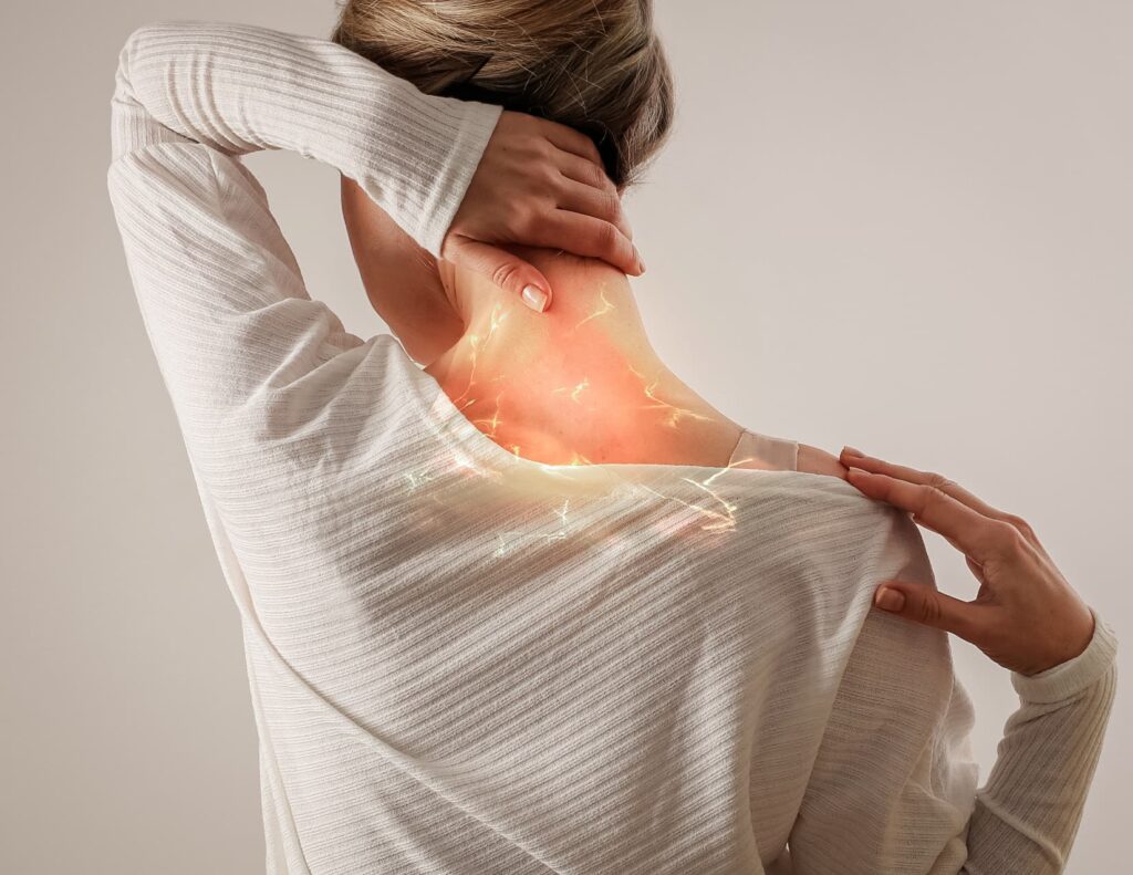 Woman facing away from the camera massages where her neck meets her head. The area is highlighted with a red glow.