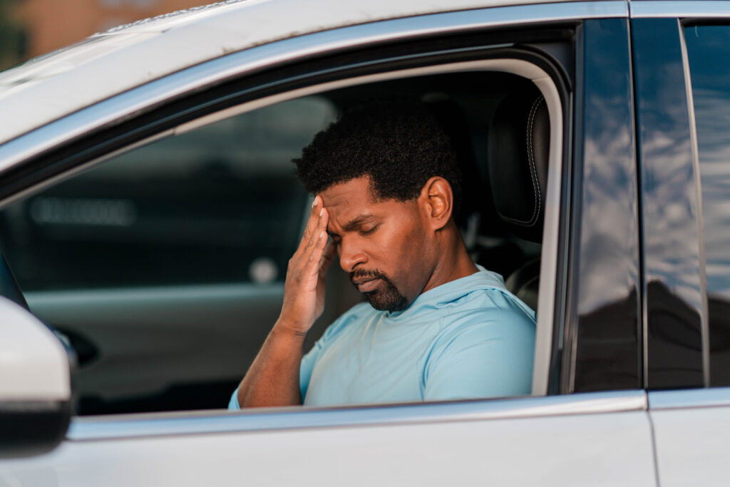 Man both stressed and in pain sits in his vehicle after a crash.