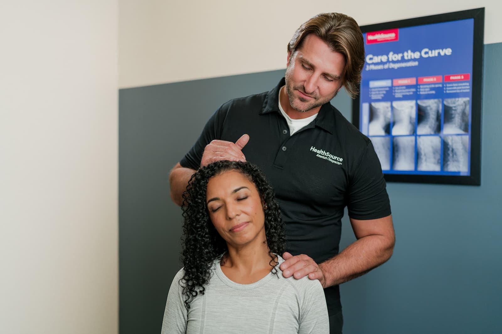 HealthSource chiropractor stands behind patient, tilting her head to the right.