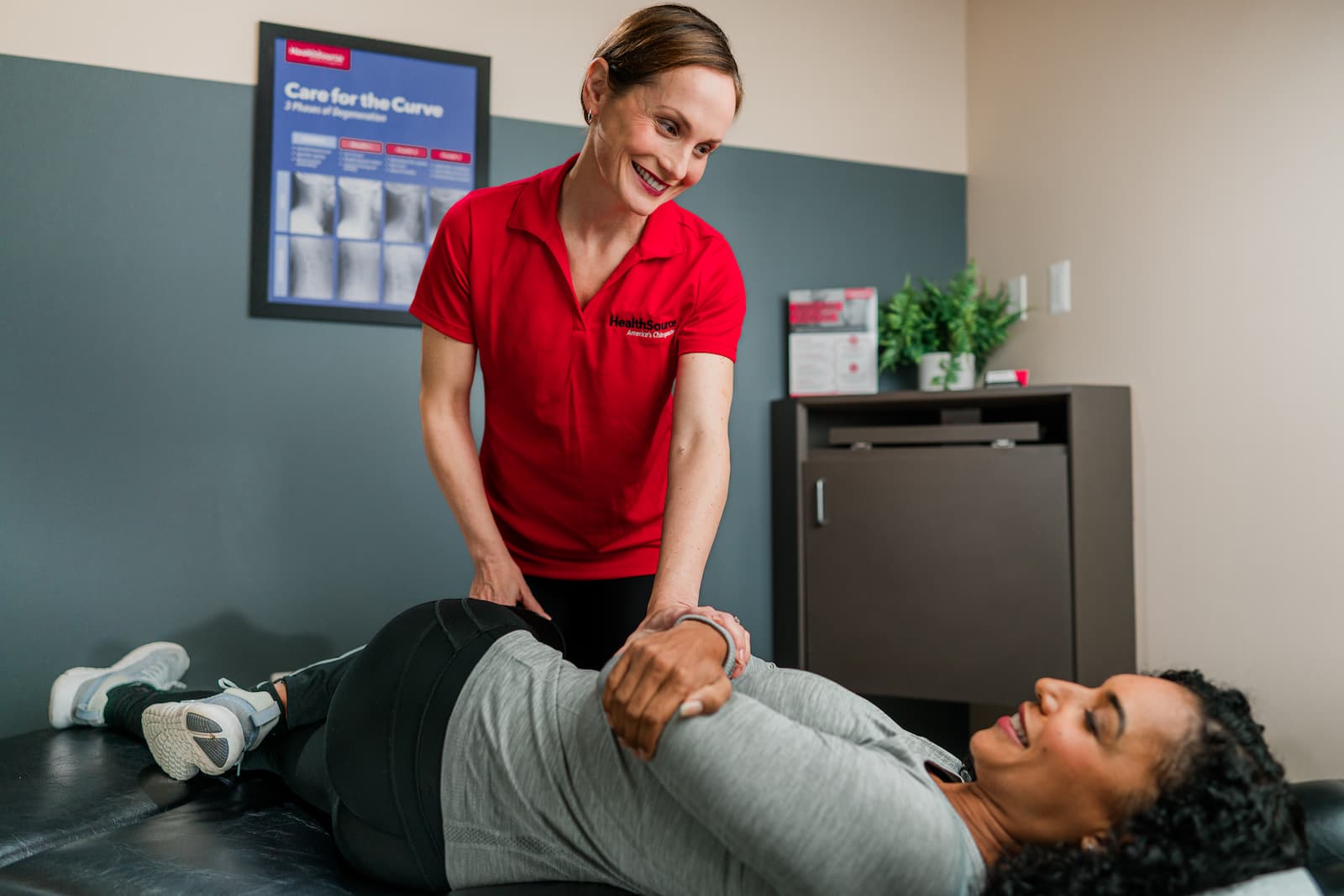 A chiropractor helps a patient laying on a table to safely twist their back to the left.