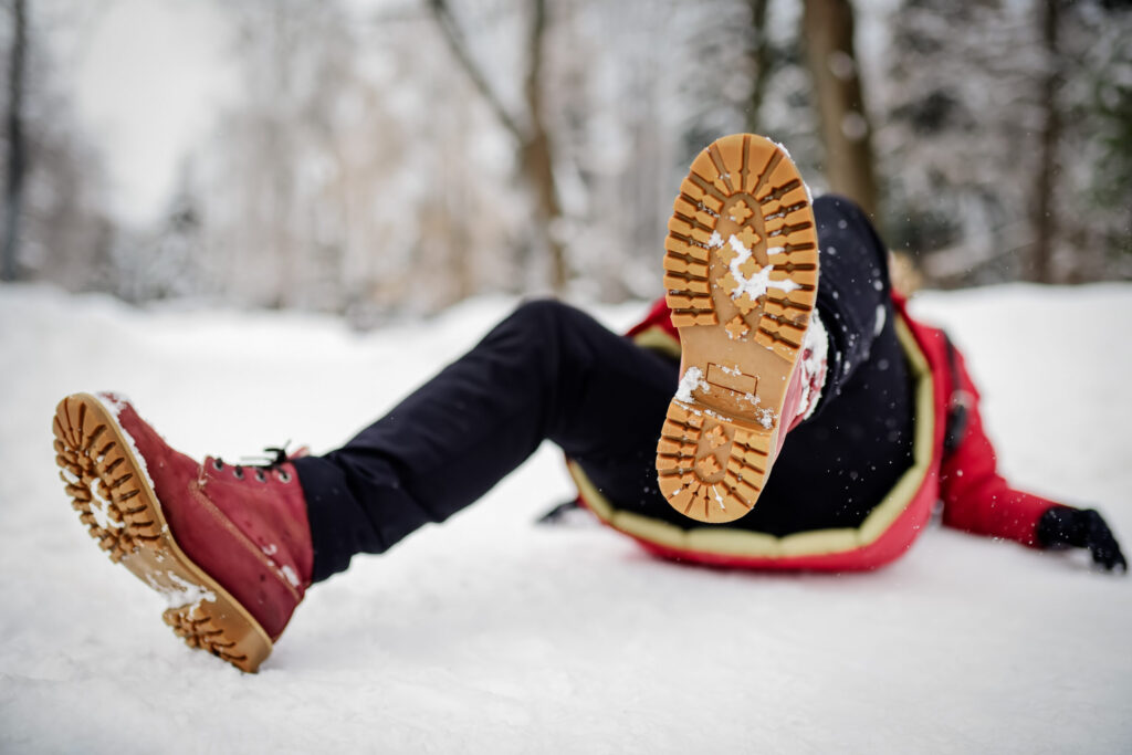 A person's boot faces us as they've fallen on snowy ground, away from the camera.