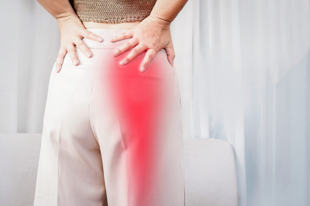 Woman holds her hands to her lower back. A red area highlights where sciatic pain typically occurs.