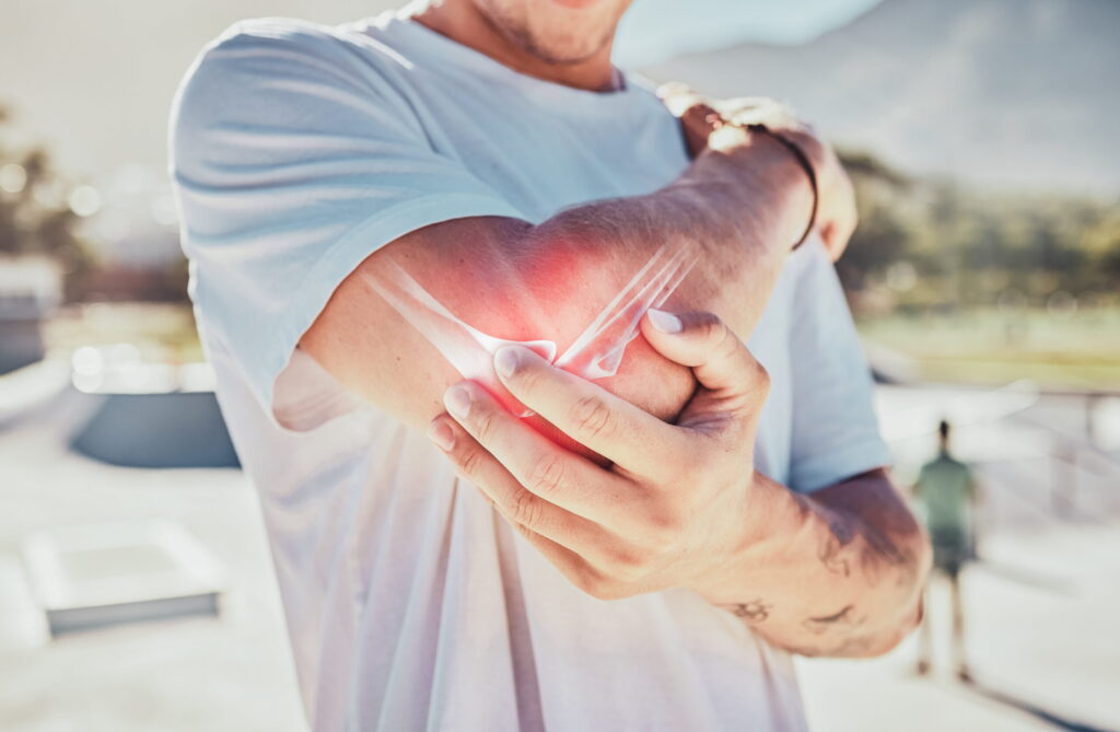 Close up shot of a man holding his elbow experiencing extremity pain. A skeletal diagram of the elbow is visible, highlighting common pain areas.