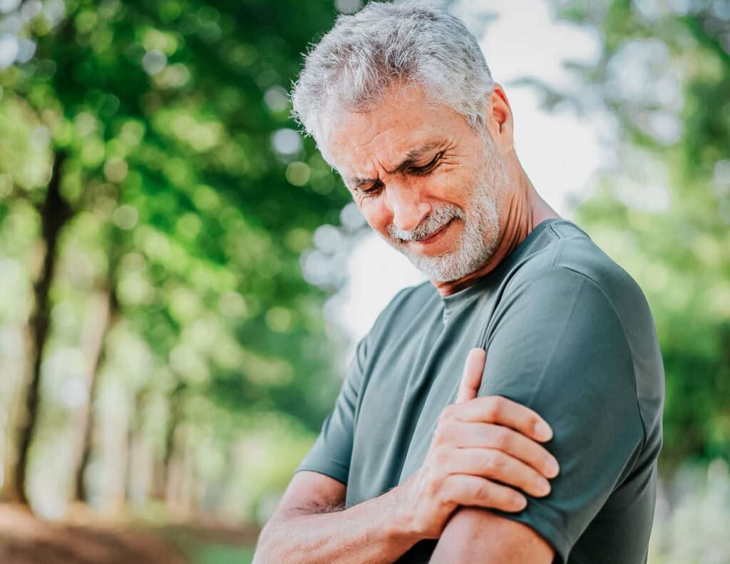 Man holds hand over left shoulder, grimacing with pain.