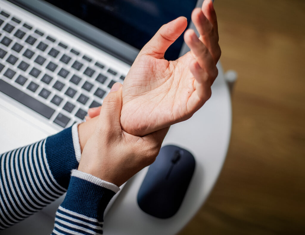 Office employee holds their wrist, working through hand pain caused by long-term keyboard use.