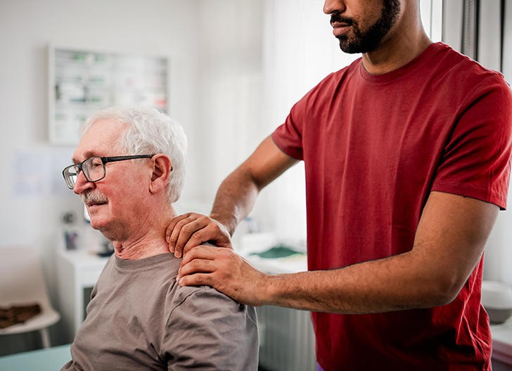 Chiropractor rubbing older man's shoulder to help with pain.