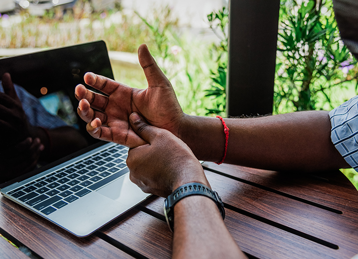 Man sitting at computer massages hand to alleviate carpal tunnel pain.