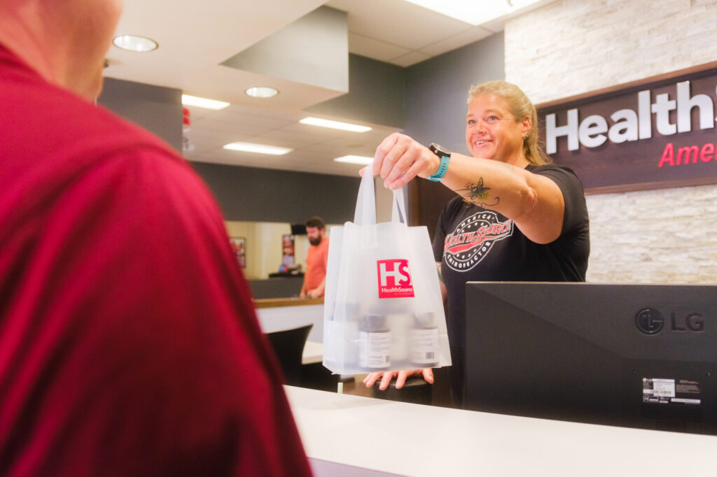 Front desk specialist handing a patient a bag of nutritional products at HealthSource of Avon