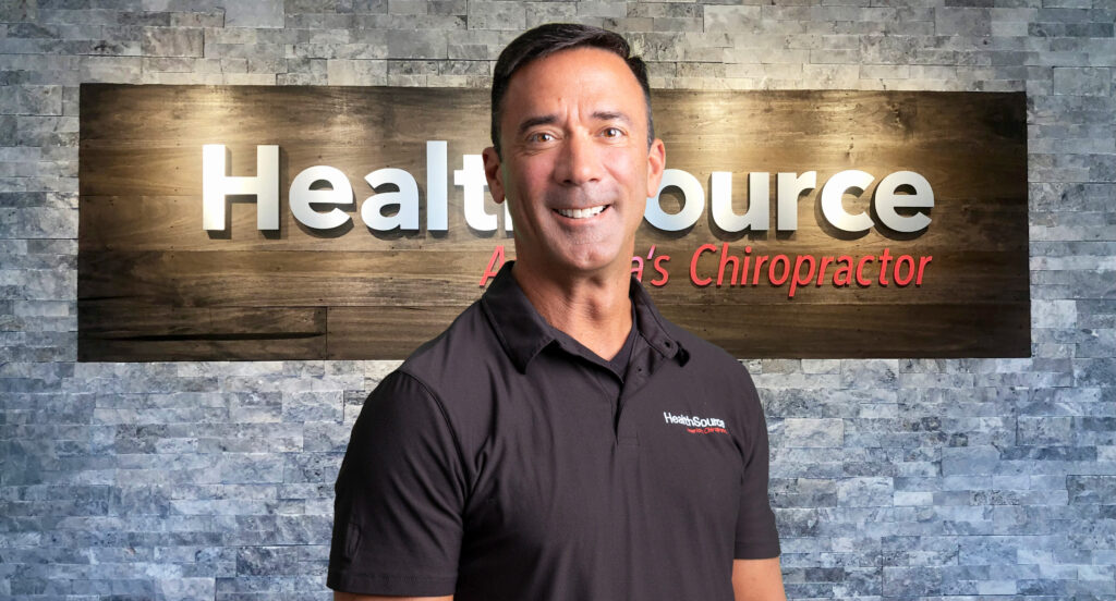 Portrait of Dr. Chris Tomshack in front of a HealthSource sign on a brick facade.