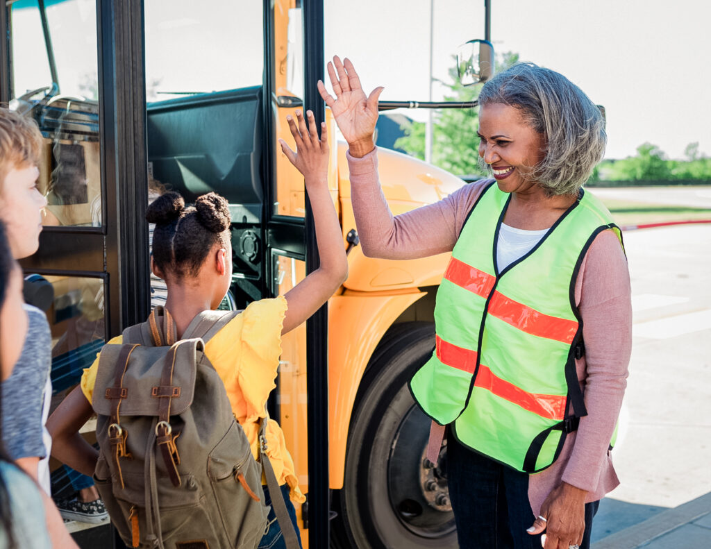 Bus driver giving high five to child that's ready to aboard school bus.