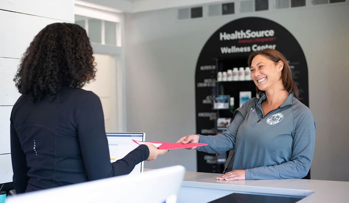 Employee behind a desk hands a patient an informational packet.