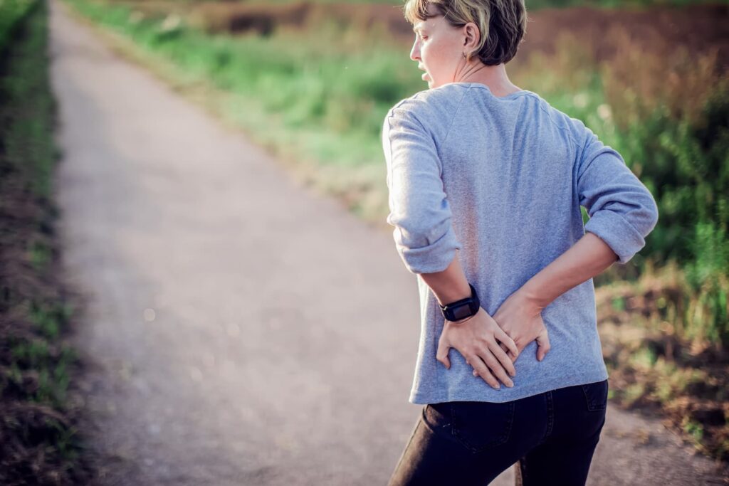 Runner stands on the edge of a trail, gripping their hip with both hands.