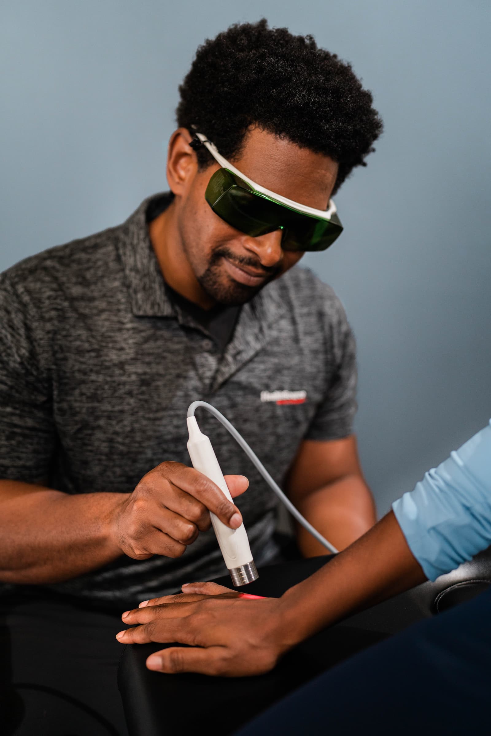 Practitioner in protective eye gear applies laser treatment to a patient's hand.