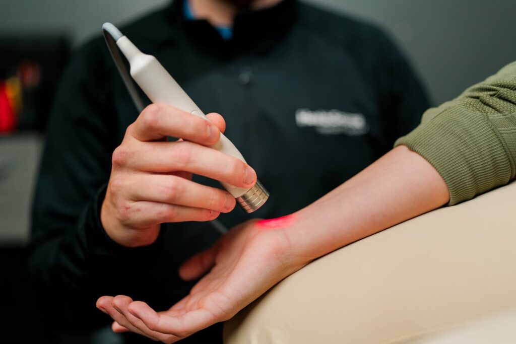 Close up of practitioner applying laser treatment to patient's wrist.