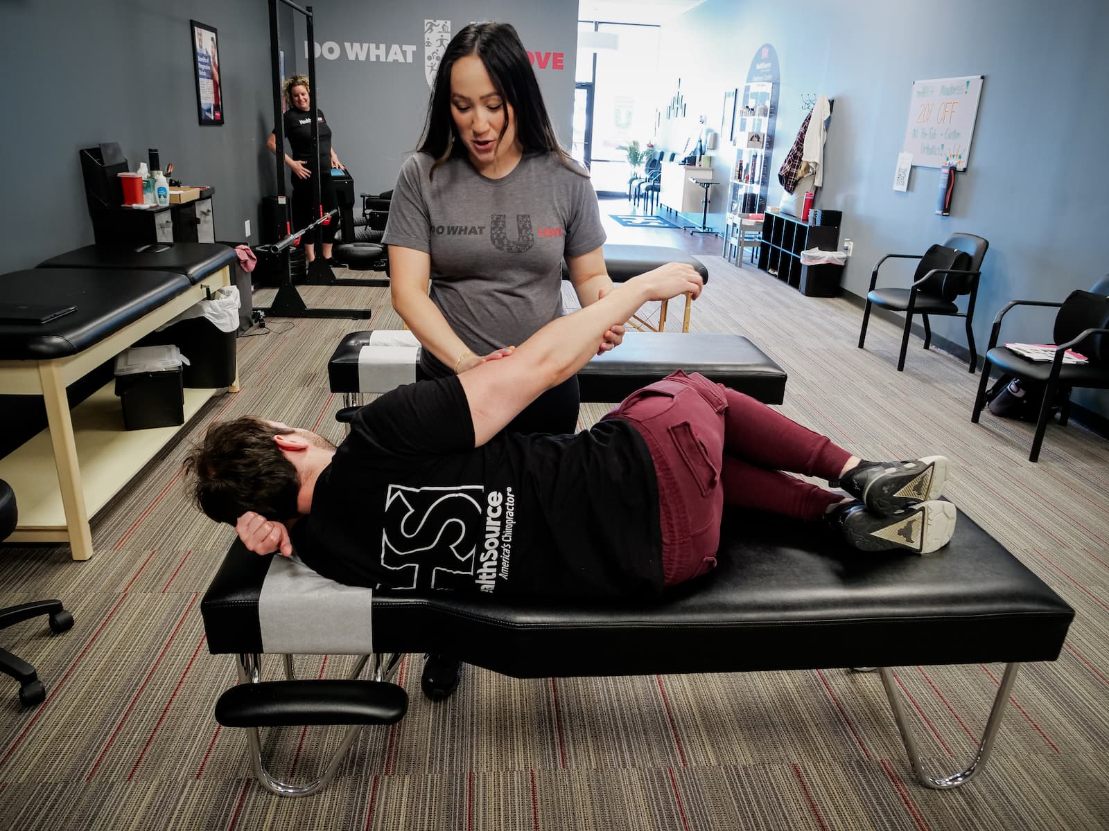 Patient lays on their side on exercise equipment. A HealthSource practitioner adjusts their right arm.