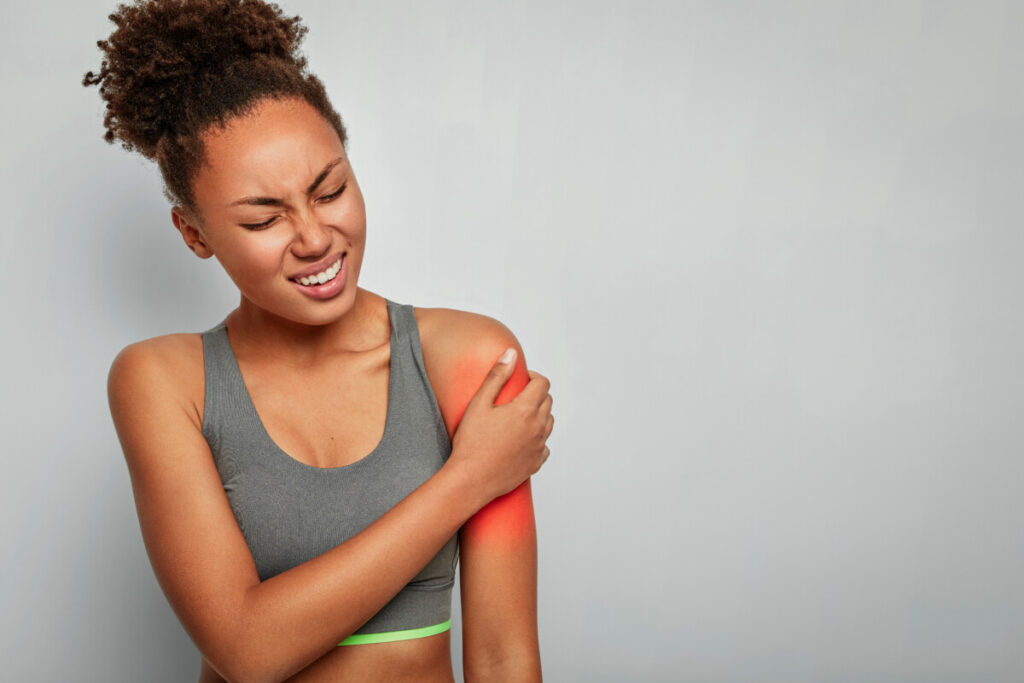 Young woman in pain wearing athletic gear holder upper bicep area, highlight red to indicate pain