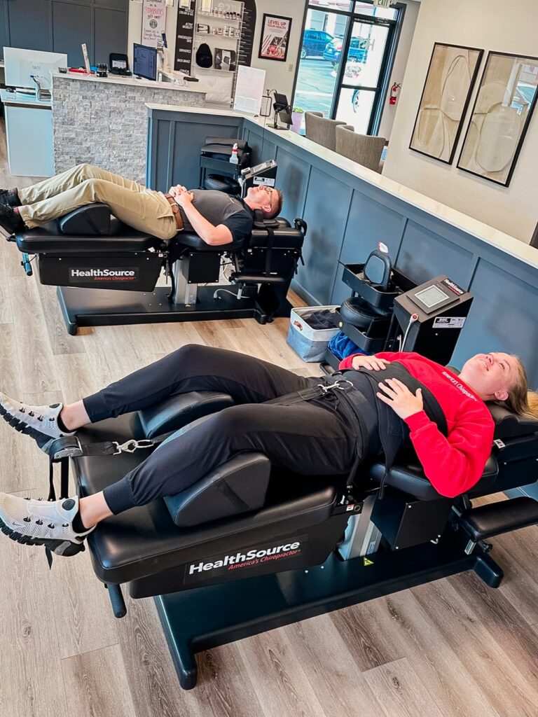 Two patients lay side-by-side on spinal decompression tables.