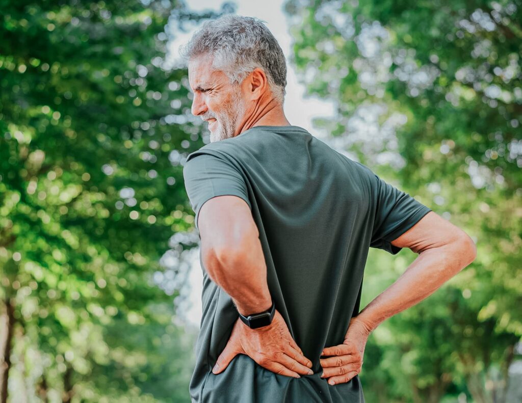 Older man presses on his lower back, grimacing in pain.