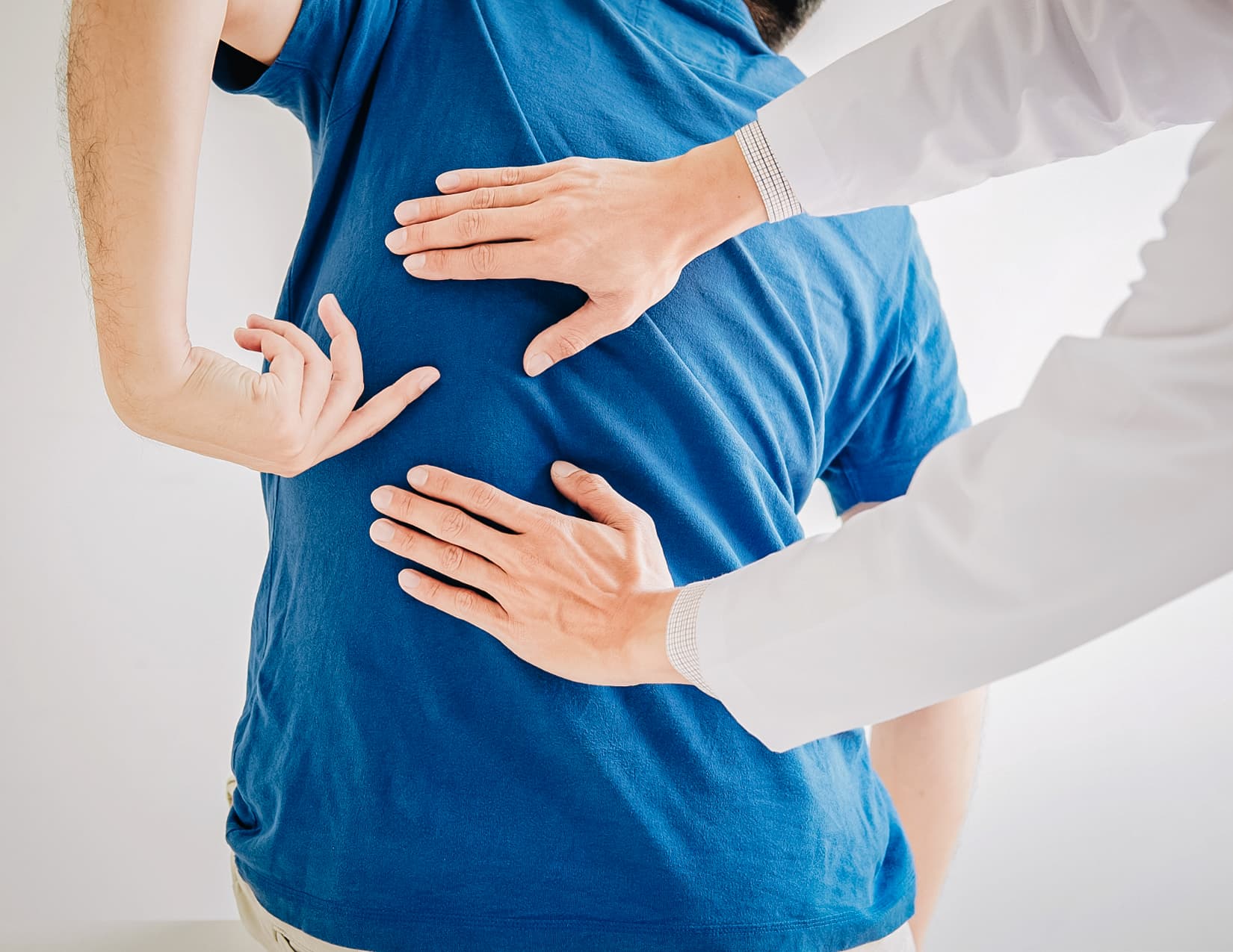 A patient points to their middle back as a practitioner presses on the same spot.