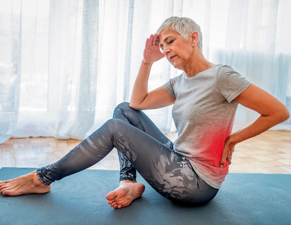 Person doing yoga pauses to hold their lower back, looking frustrated and tired.