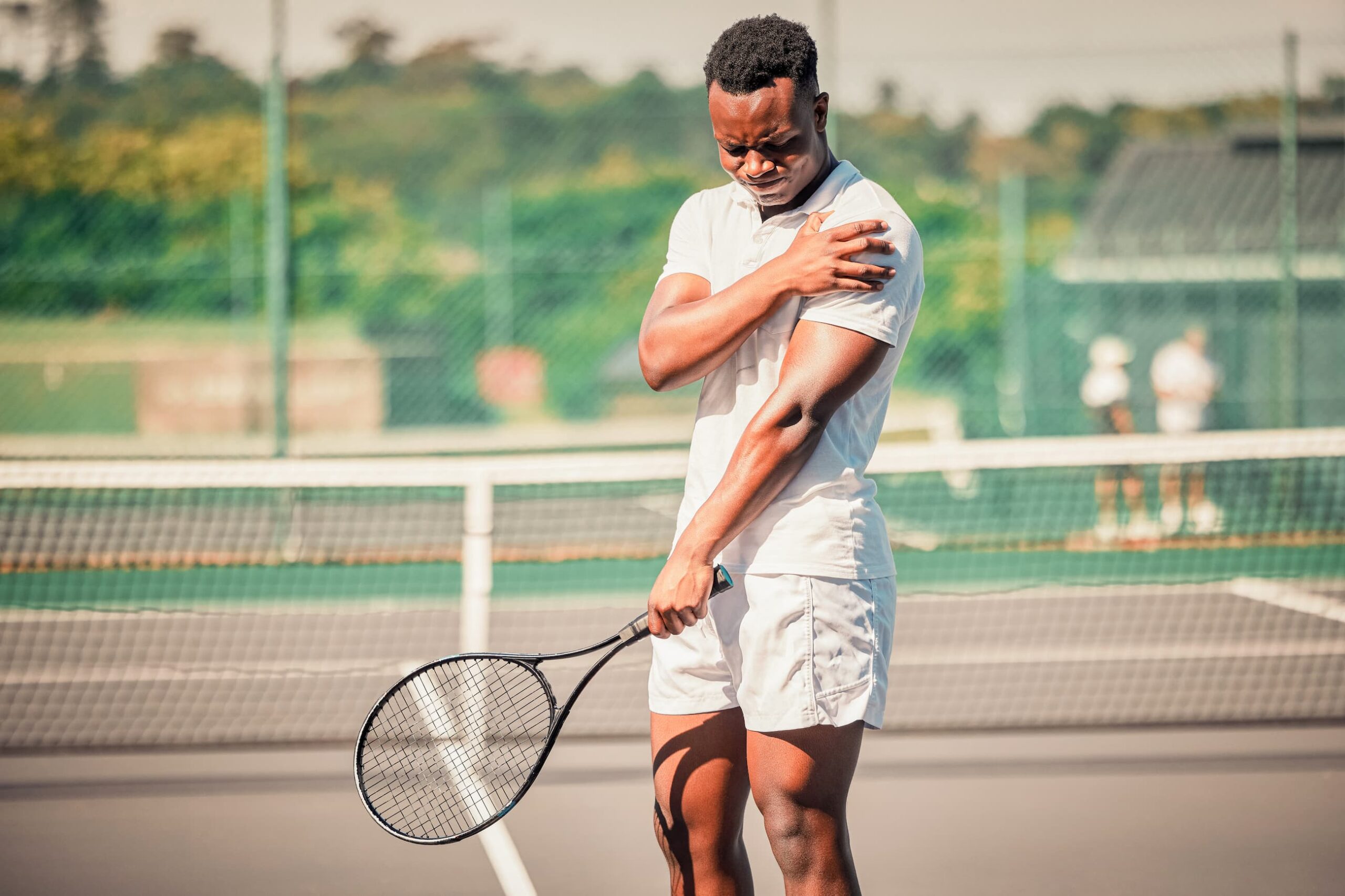 Male tennis player pauses the game, grimacing as he holds his injured shoulder.