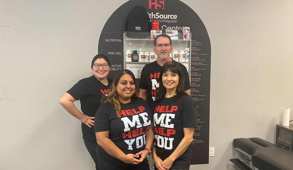 The team at HealthSource of Atascocita posing together in front of the HealthSource Wellness Wall.